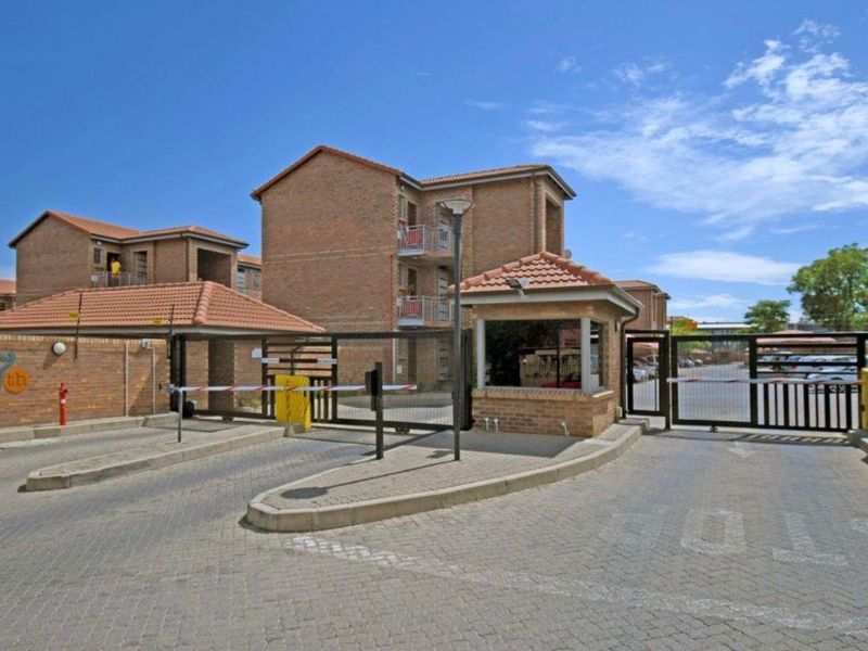 The secure entrance to the apartment complex features a brick guard house, automated boom gates, and perimeter fencing for controlled access.