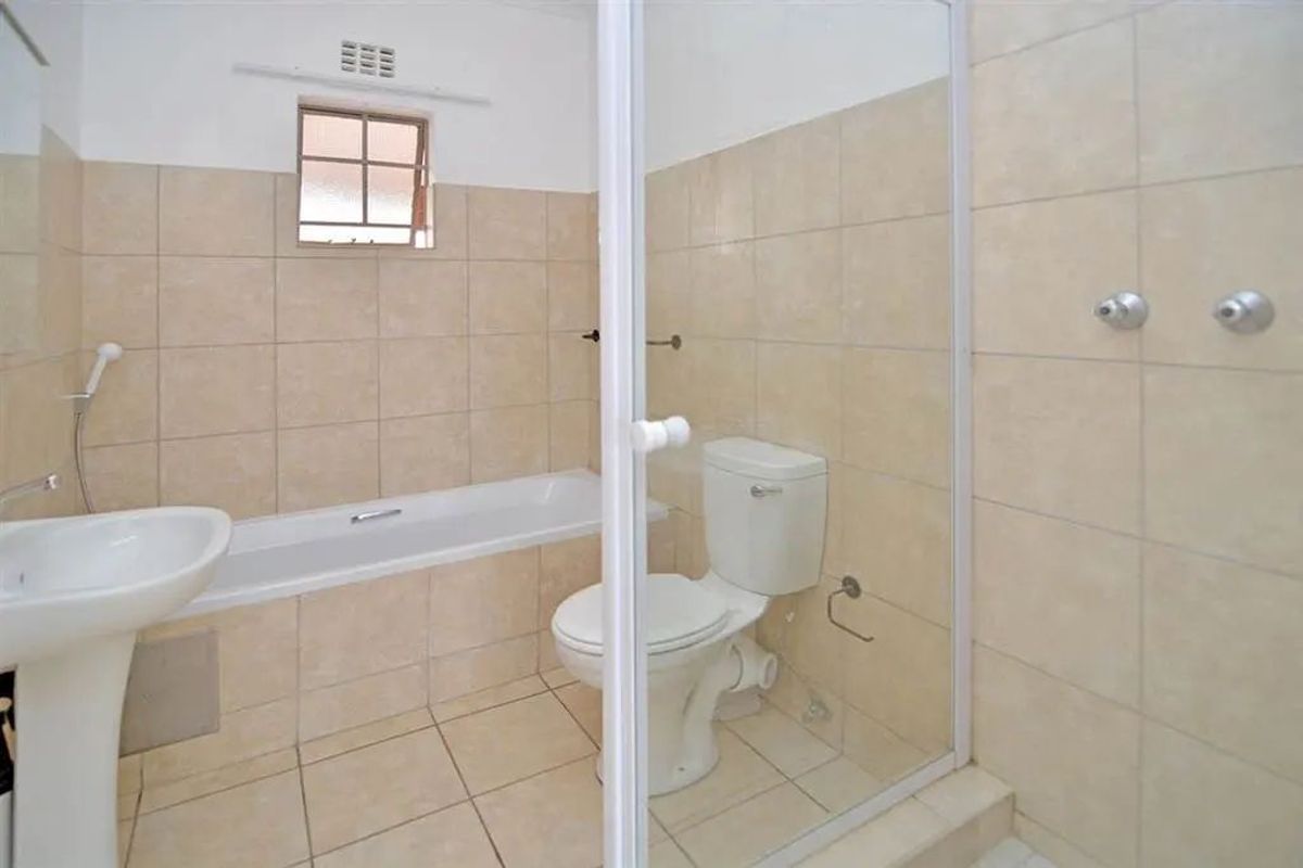 A functional bathroom featuring a pedestal basin, bathtub, and a separate shower enclosure with tiled walls and flooring.
