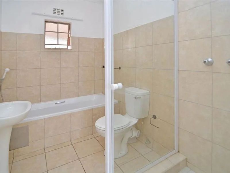 A functional bathroom featuring a pedestal basin, bathtub, and a separate shower enclosure with tiled walls and flooring.