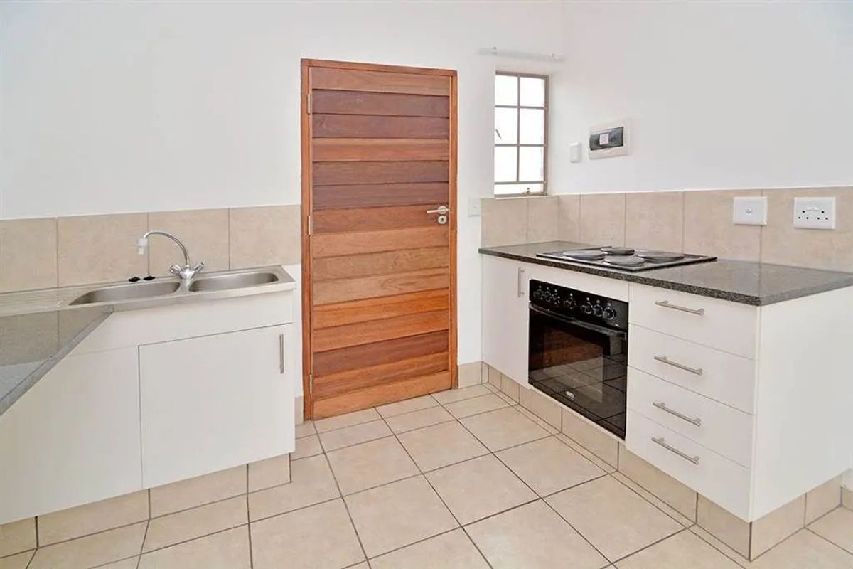 A functional kitchen featuring white cabinetry, granite countertops, a built-in oven, electric hob, and tiled flooring.