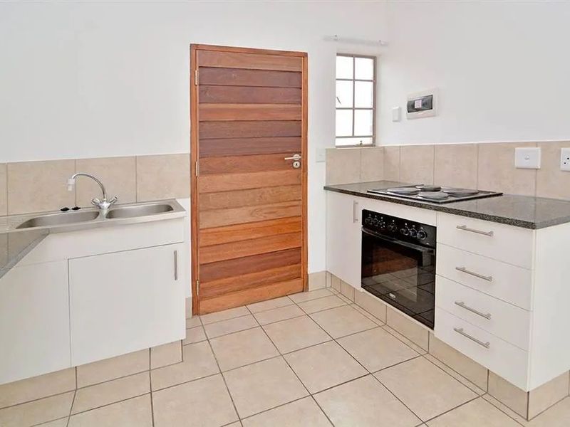 A functional kitchen featuring white cabinetry, granite countertops, a built-in oven, electric hob, and tiled flooring.