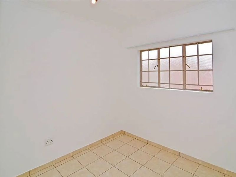 An empty bedroom featuring neutral tiled flooring and a metal-framed window, providing a blank canvas for personalization.