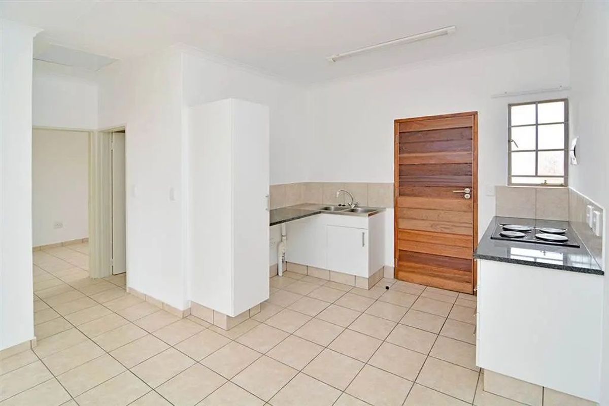 A functional, empty kitchen featuring tiled flooring, granite countertops, built-in cabinetry, and a built-in hob, offering a clean and neutral space.