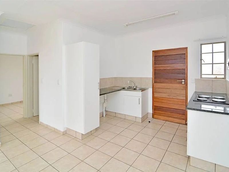 A functional, empty kitchen featuring tiled flooring, granite countertops, built-in cabinetry, and a built-in hob, offering a clean and neutral space.