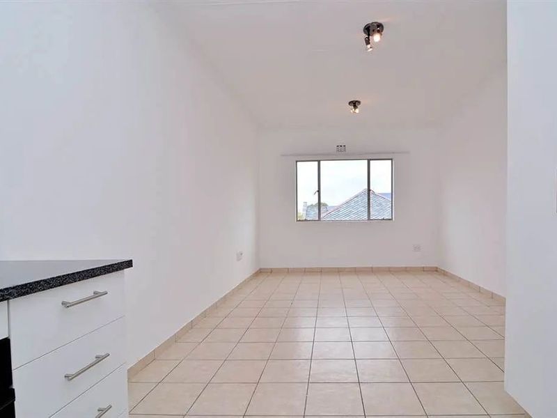 A bright, empty open-plan living and kitchen area featuring tiled flooring, modern white cabinetry, and granite countertops with a view through the window.