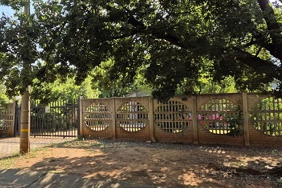 Front view of the property featuring a decorative precast concrete boundary wall and metal security gate, partially shaded by a large mature tree.