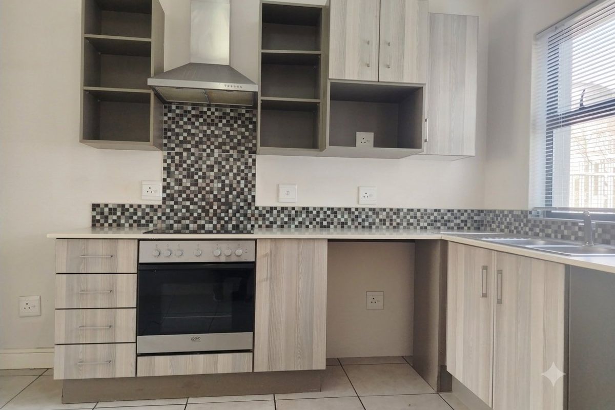 Modern kitchen featuring light wood-grain cabinetry, mosaic tile backsplash, built-in oven with extractor fan, and tiled flooring in a clean, functional layout.