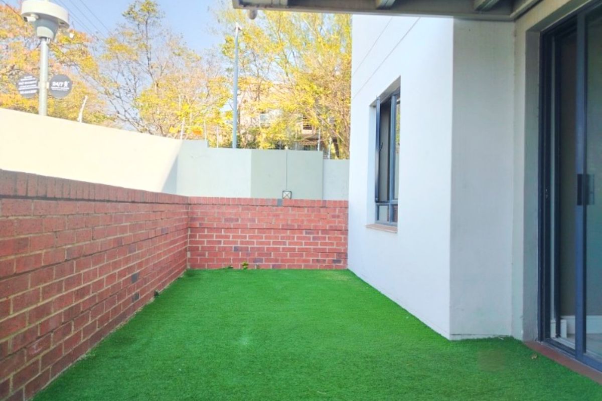 A private rear courtyard featuring a brick boundary wall, artificial lawn, and direct access to the interior via a sliding glass door.