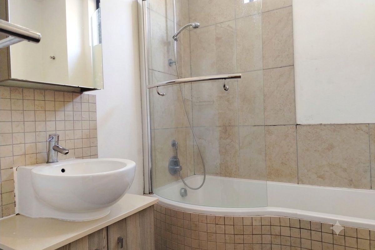 A functional bathroom featuring a curved bathtub with a glass shower screen, a vessel sink vanity, and neutral tiled finishes.
