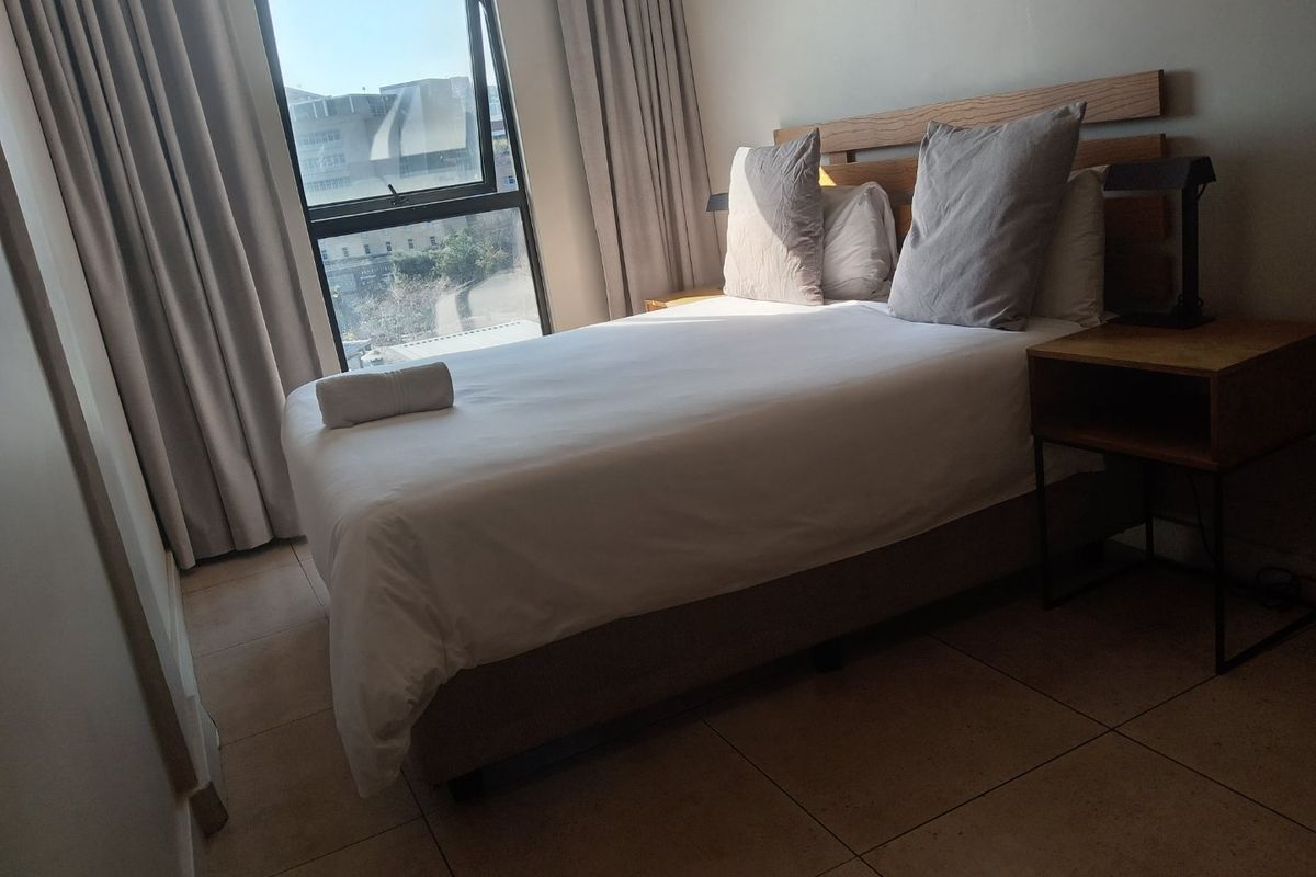 A well-lit bedroom featuring tiled flooring and a large window with curtain tracks, offering a clean and functional living space.