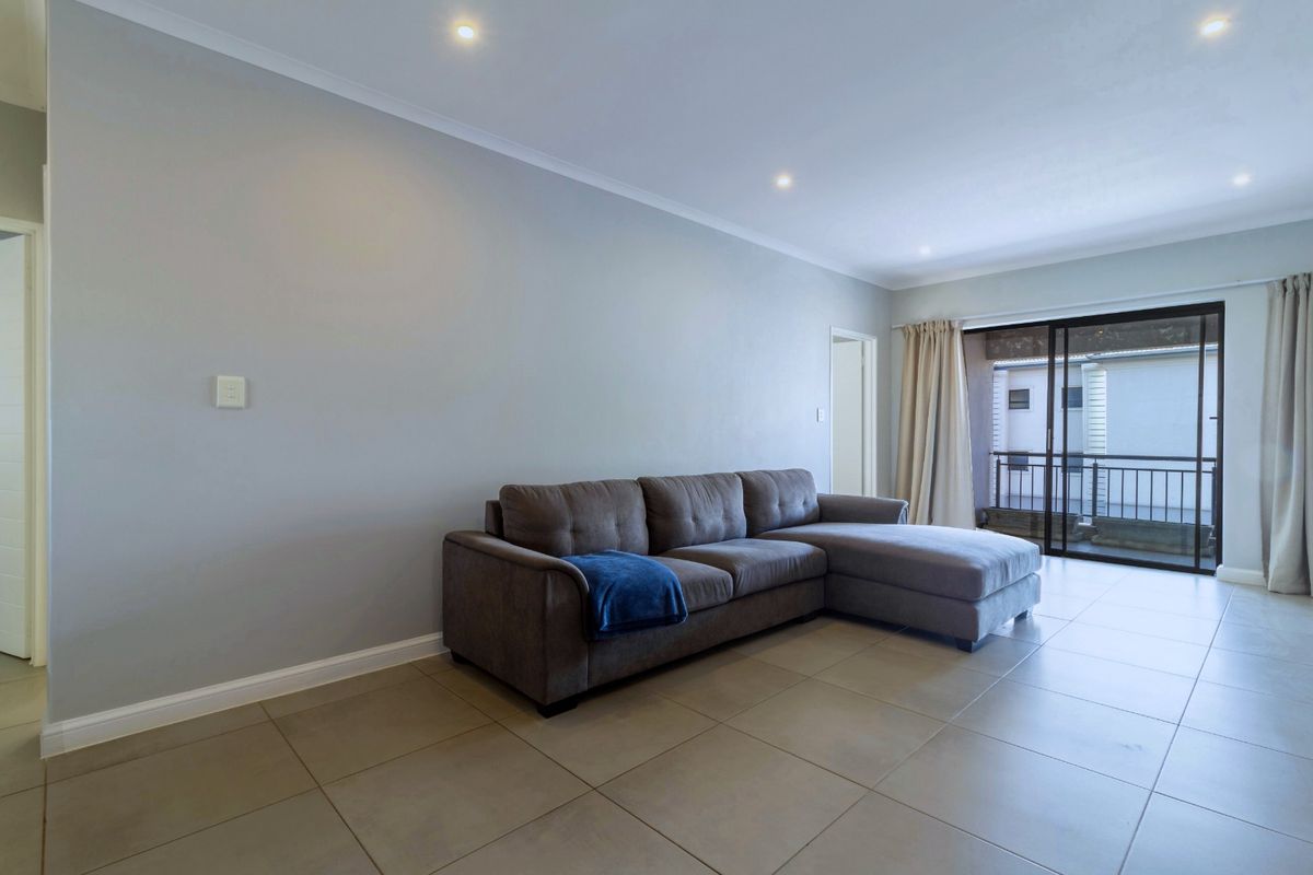A bright living room featuring neutral tiled flooring, recessed downlighting, and a sliding glass door providing access to an attached balcony.