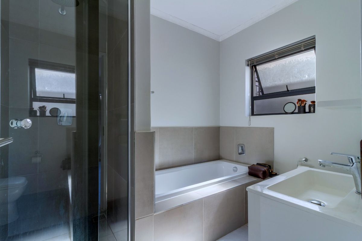 Modern bathroom featuring a glass-enclosed shower, a built-in bathtub with tiled surround, and a sleek vanity basin with contemporary mixer taps.
