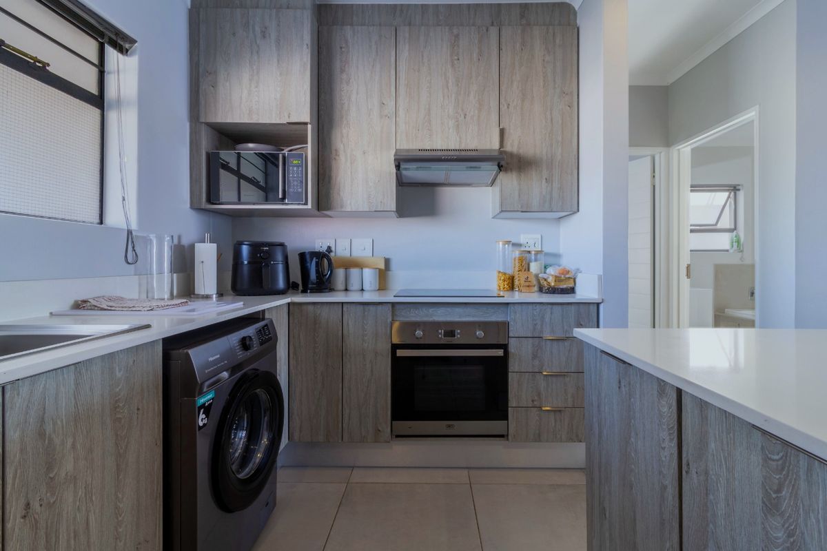 Modern kitchen featuring wood-grain cabinetry, stone countertops, integrated appliances, and a built-in oven and hob, offering a clean and functional workspace.