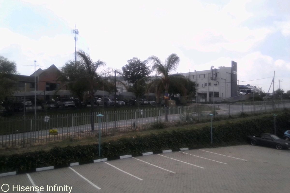 Exterior view of a commercial property featuring a paved parking area, security fencing, and surrounding landscaped grounds.