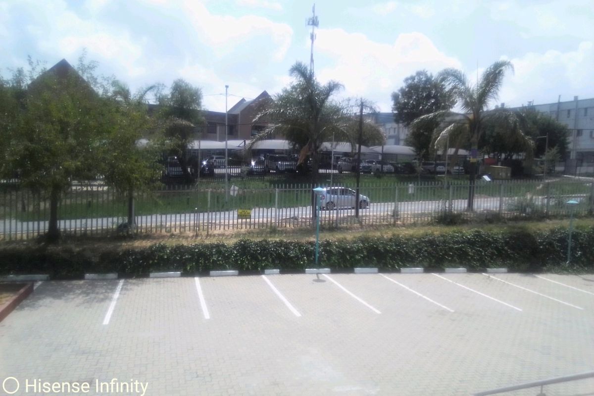 An elevated view overlooking a paved commercial parking area, security fencing, and surrounding landscaped grounds.