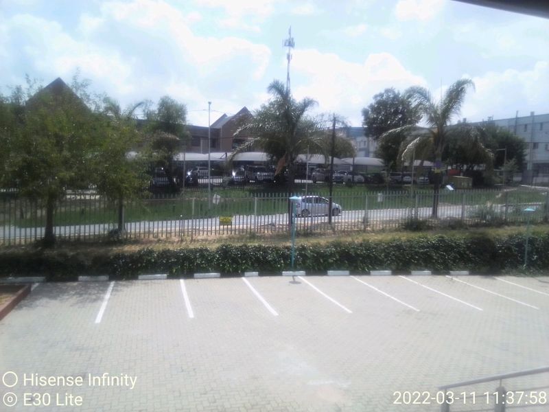 An elevated view overlooking a paved commercial parking area, security fencing, and surrounding landscaped grounds.