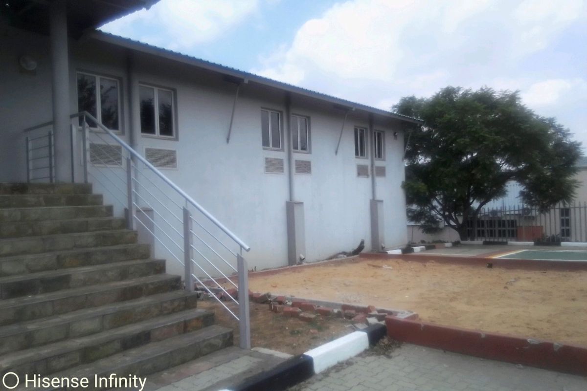 Rear exterior view of a commercial building featuring a concrete staircase with metal railings, paved areas, and a sand pit.