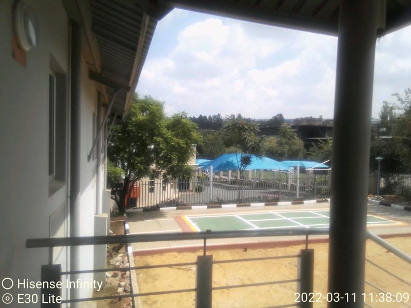 A view from a balcony overlooking a paved courtyard area featuring a sports court and blue shade sails.