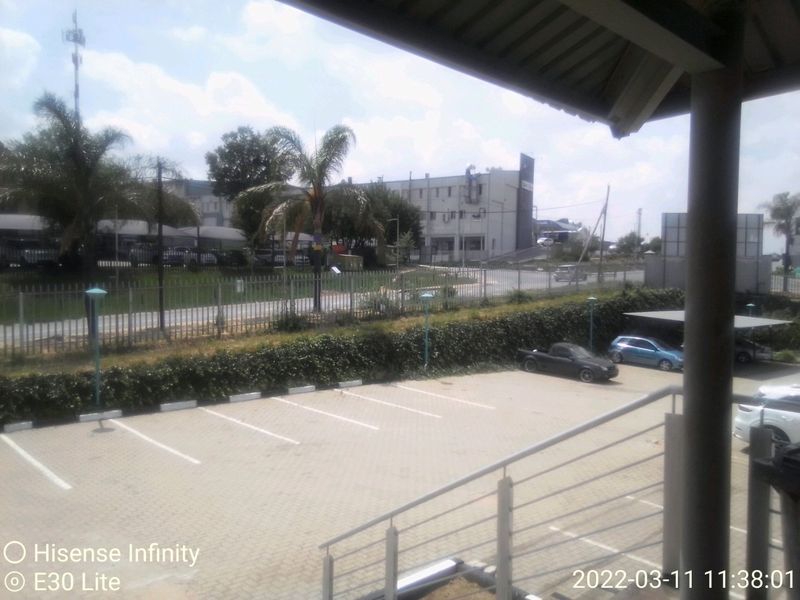 An elevated view overlooking a paved commercial parking lot with covered bays and surrounding perimeter fencing.