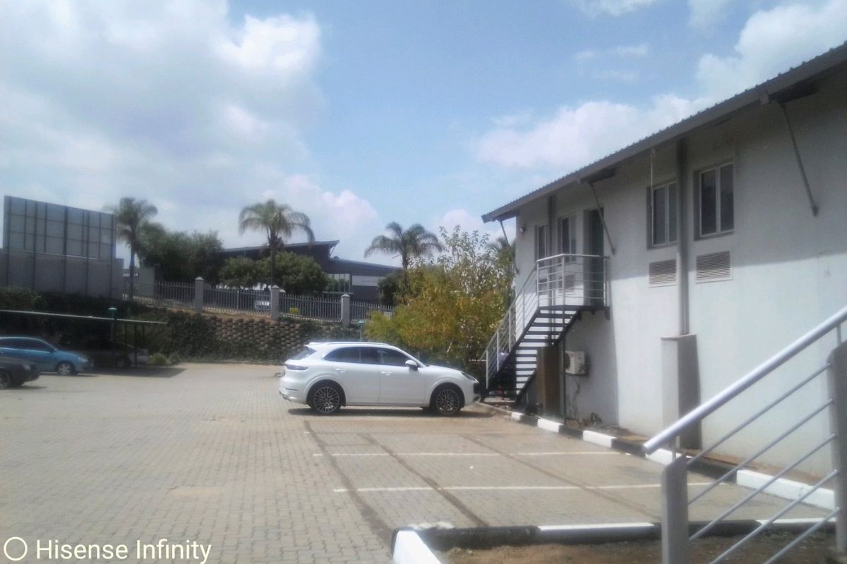 Exterior view of a commercial building featuring a paved parking area, external staircase access, and perimeter security fencing.