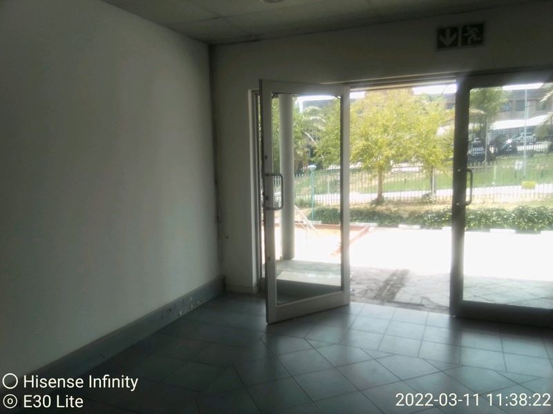 An empty commercial entry space featuring tiled flooring, a suspended ceiling, and a glass door leading to an outdoor area.