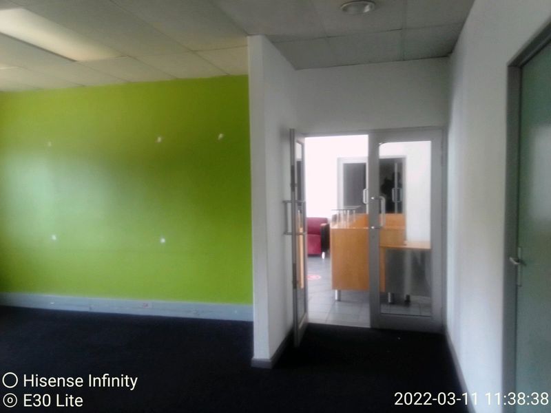An empty office space featuring a lime green accent wall, dark carpeting, and a glass partition door leading to an adjacent area.