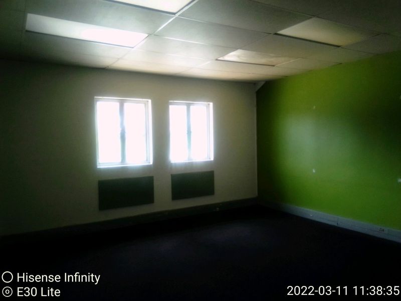 An empty commercial office space featuring a suspended ceiling, recessed lighting, carpeted flooring, and wall-mounted heating units.