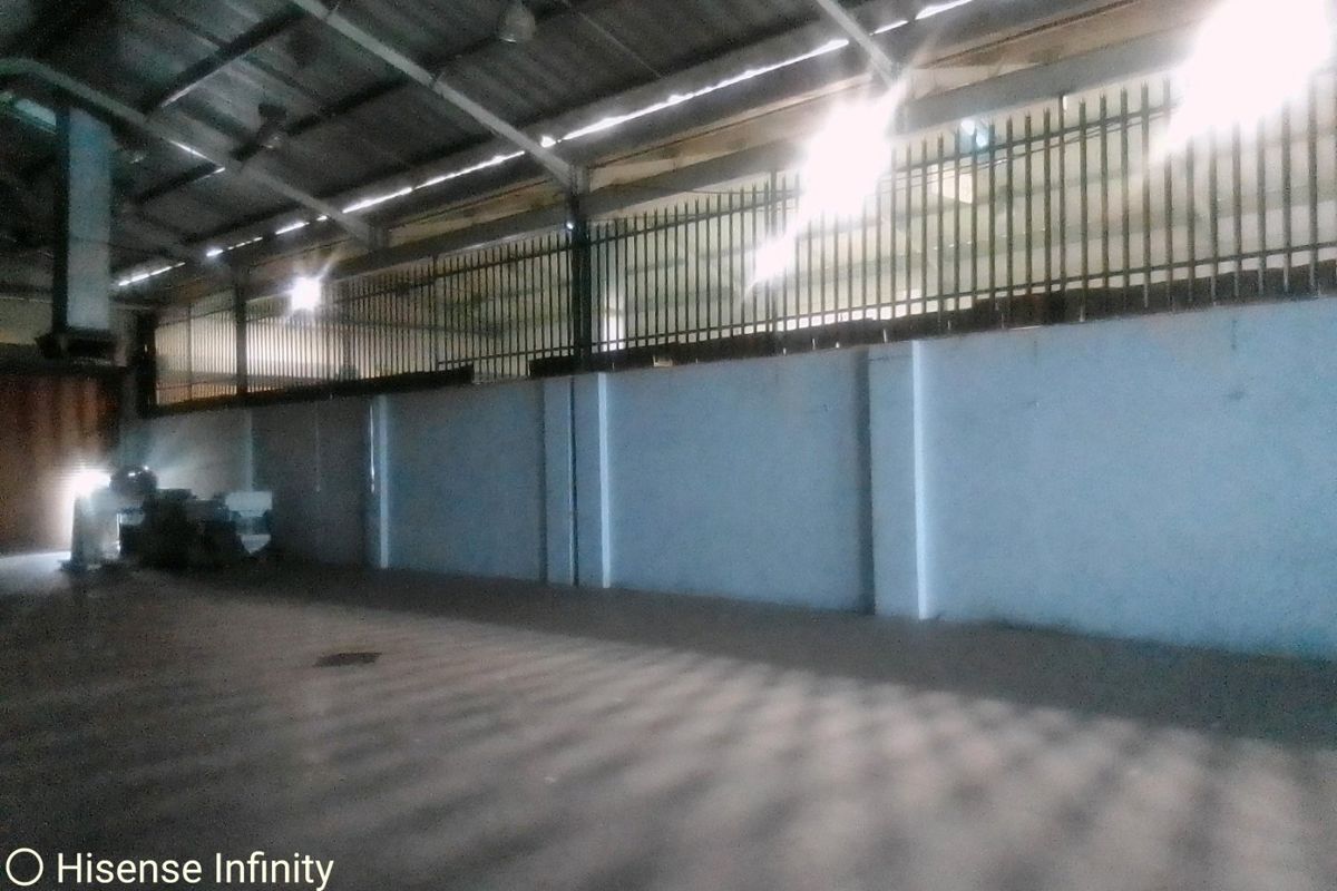 A spacious industrial utility area featuring exposed steel roof trusses, concrete flooring, and secure perimeter fencing.