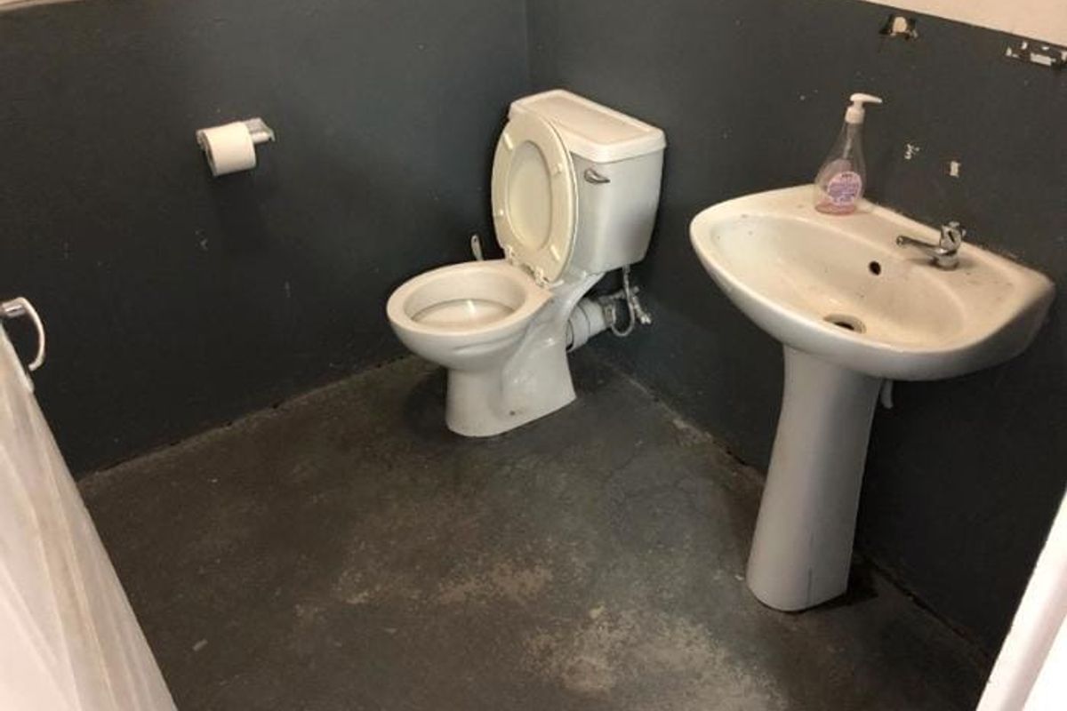 A basic industrial-style bathroom featuring a pedestal sink and toilet with unfinished wall finishes and worn flooring.