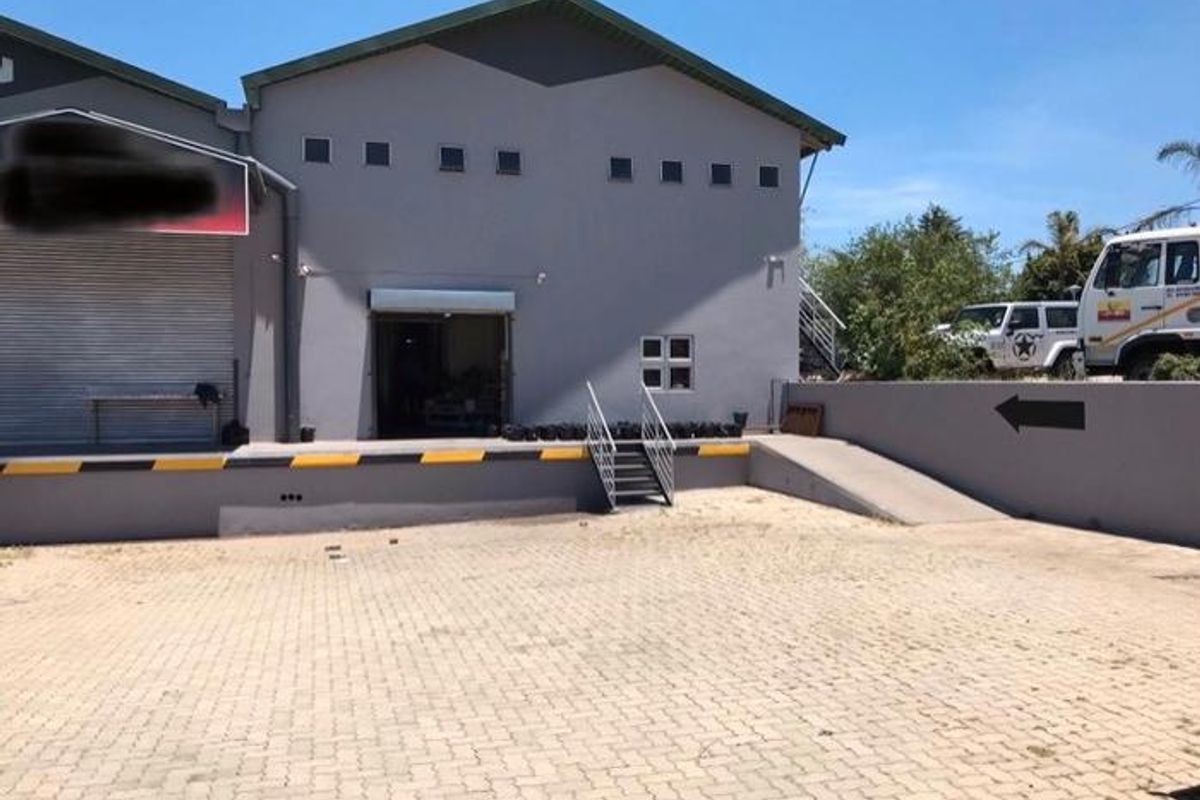 Industrial warehouse exterior featuring a loading dock, roller shutter door, and paved yard area with a retaining wall.
