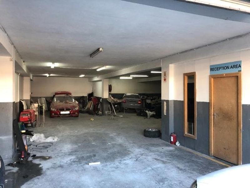 A spacious commercial garage or workshop area featuring concrete flooring, fluorescent lighting, and a designated reception entrance.