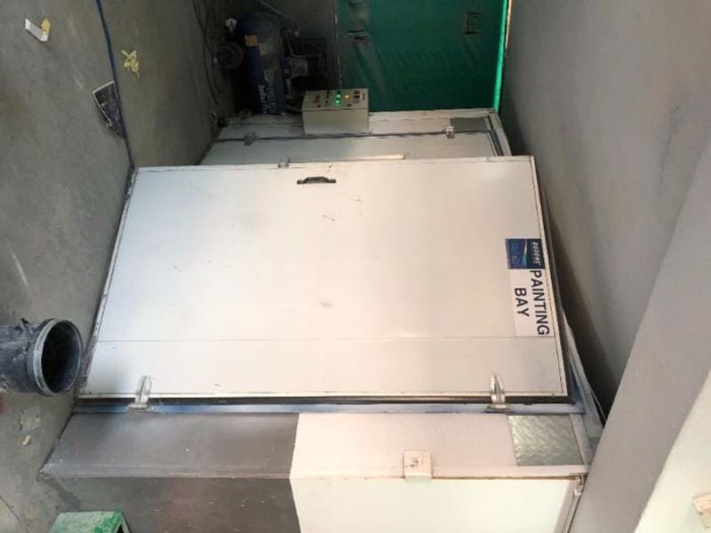 An industrial painting bay unit featuring a control panel and integrated air compressor, suitable for commercial workshop or manufacturing applications.