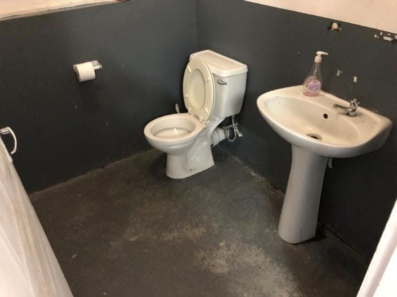 A small, basic bathroom featuring a pedestal sink and toilet, currently in need of cosmetic updates and wall repairs.