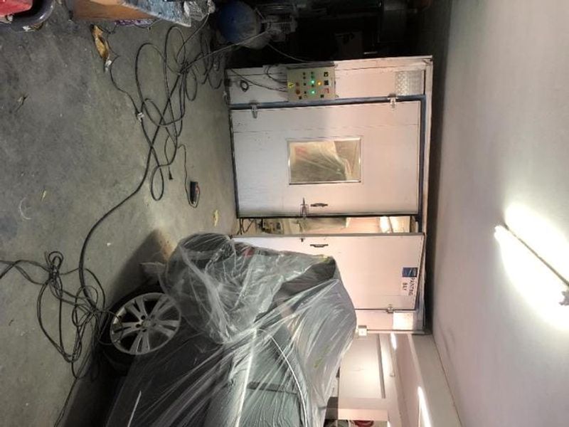Commercial utility space featuring a dedicated industrial spray booth with integrated control panel and overhead fluorescent lighting.