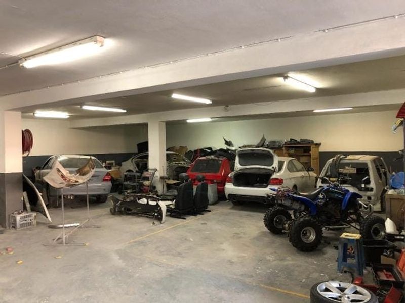 Spacious commercial garage area featuring concrete flooring, structural support columns, and overhead fluorescent lighting, currently utilized for vehicle storage and maintenance.