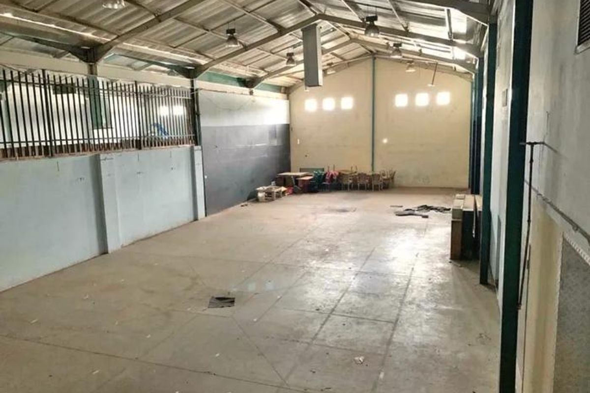 Spacious industrial utility area featuring exposed steel roof trusses, concrete flooring, and high-level windows, suitable for storage or workshop use.