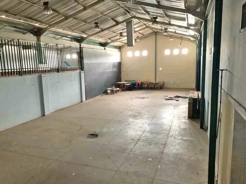 Spacious industrial utility area featuring exposed steel roof trusses, concrete flooring, and high-level windows, suitable for storage or workshop use.
