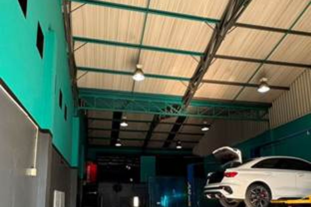 A spacious commercial garage facility featuring high ceilings with exposed steel trusses, industrial lighting, and a dedicated vehicle service lift area.