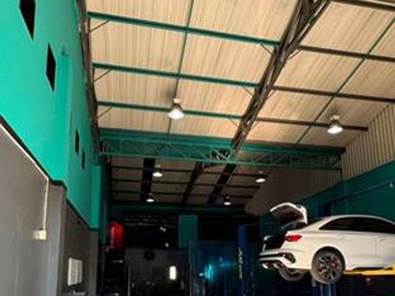 A spacious commercial garage facility featuring high ceilings with exposed steel trusses, industrial lighting, and a dedicated vehicle service lift area.