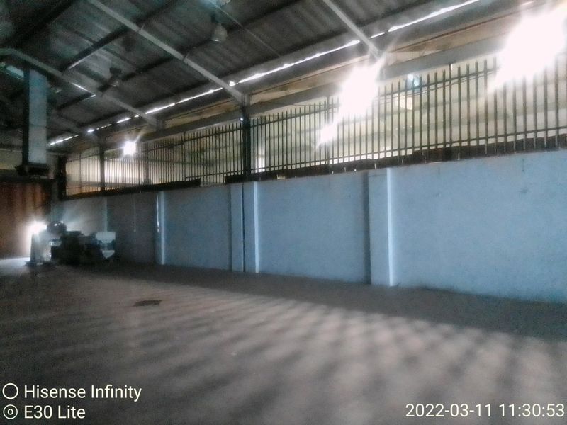 A large, open-plan industrial utility space featuring high ceilings with exposed steel beams, concrete flooring, and perimeter security fencing.