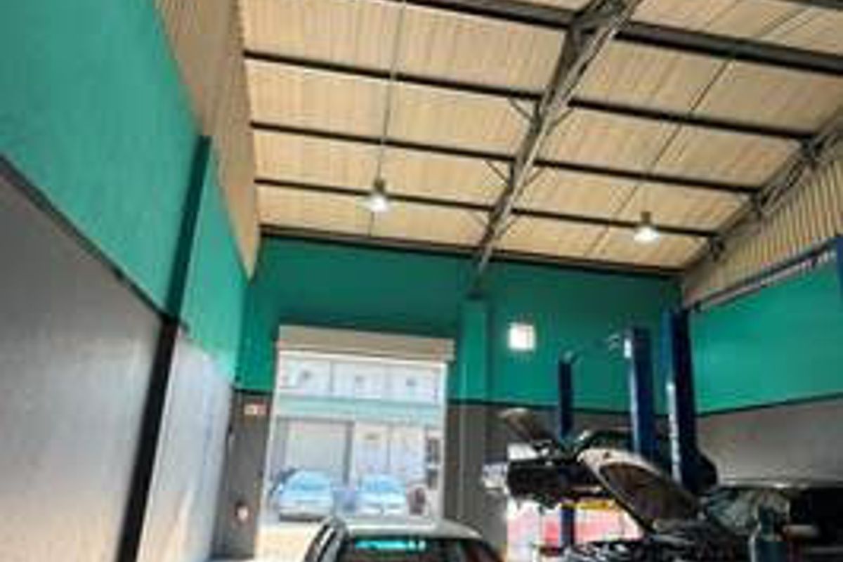 Spacious commercial garage featuring high ceilings with exposed steel trusses, concrete flooring, and an integrated vehicle service lift for automotive maintenance.