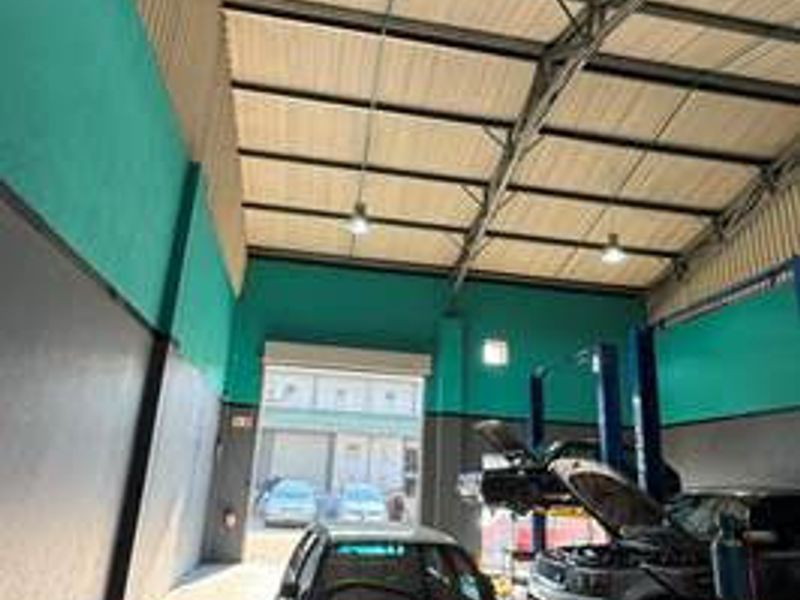 Spacious commercial garage featuring high ceilings with exposed steel trusses, concrete flooring, and an integrated vehicle service lift for automotive maintenance.