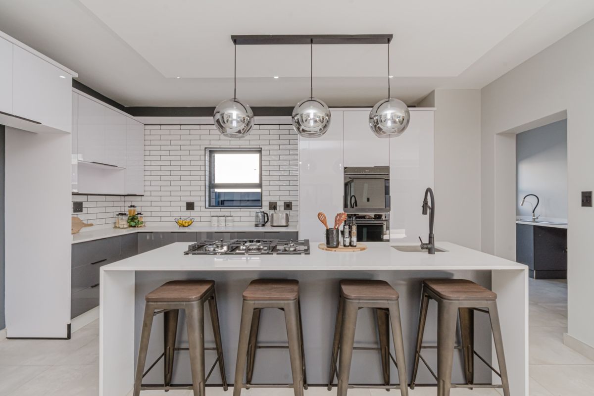 Modern kitchen featuring a central island with a gas hob, sleek white and grey cabinetry, subway tile backsplash, and high-end finishes.