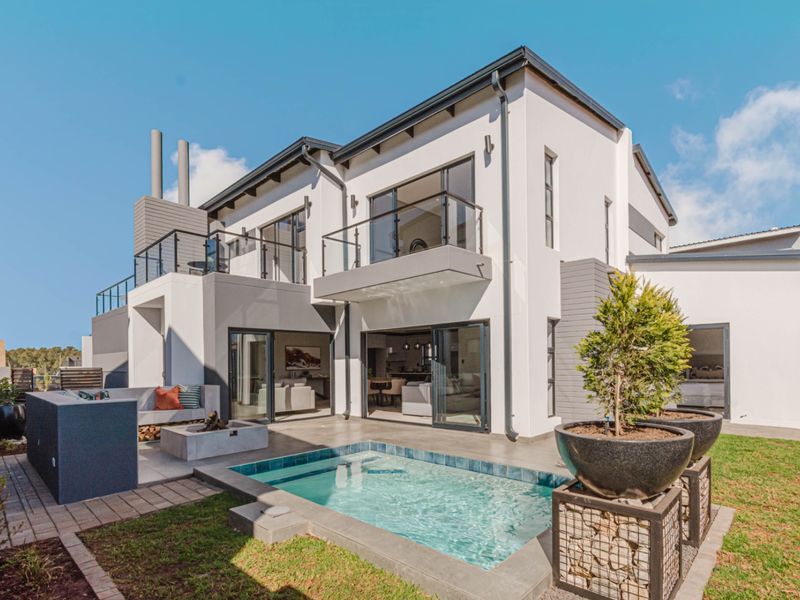 Modern double-story rear elevation featuring a swimming pool, paved patio area, built-in braai, and upper-level balconies with glass balustrades.