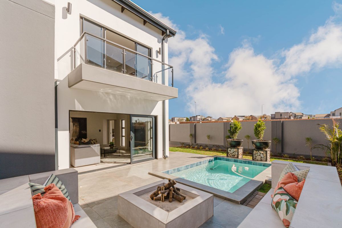 Rear exterior view featuring a modern patio with a built-in fire pit, a swimming pool, and an upper-level balcony with glass balustrades.