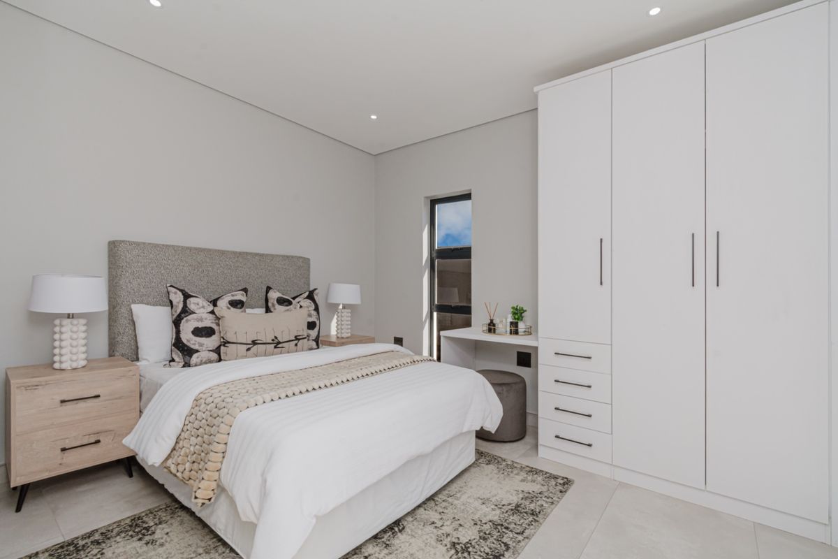 A modern, well-lit bedroom featuring neutral tones, tiled flooring, a built-in wardrobe with integrated drawers, and recessed ceiling lighting.