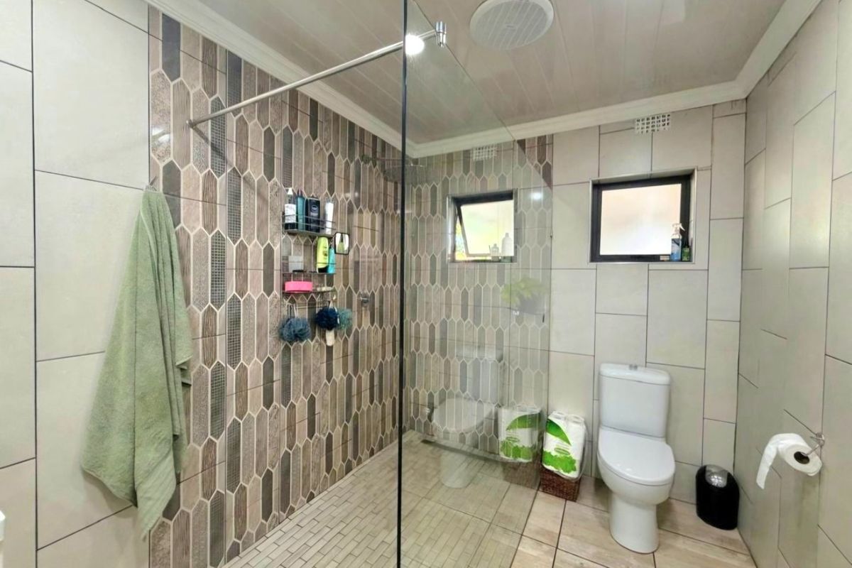 Modern bathroom featuring a spacious walk-in shower with glass screen, decorative tiled accent wall, and neutral floor tiles.