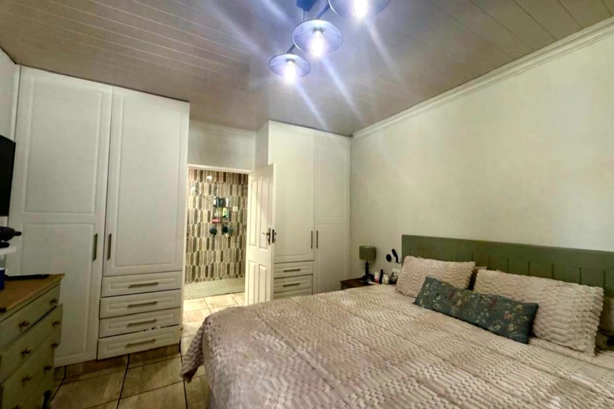 A well-maintained bedroom featuring built-in wardrobes, tiled flooring, and a tongue and groove ceiling, with direct access to an en-suite bathroom.