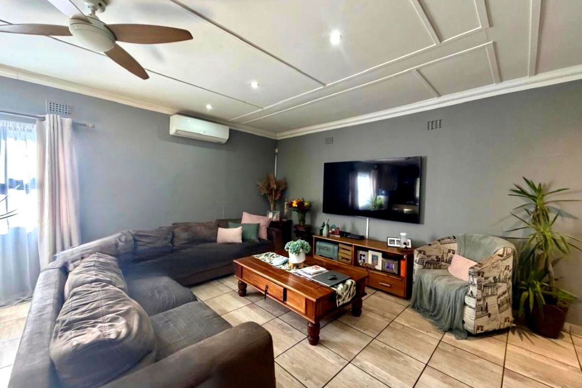 A comfortable living room featuring tiled flooring, decorative ceiling molding, a ceiling fan, and a wall-mounted split-system air conditioner.