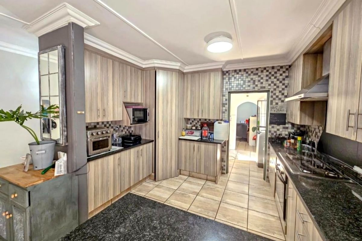 A functional kitchen featuring wood-look cabinetry, granite countertops, mosaic tile backsplash, and built-in appliances, offering a practical layout for daily cooking.